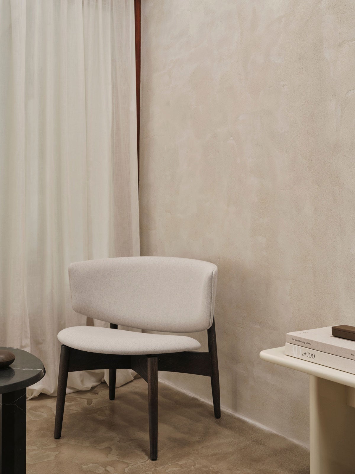 Herman Loungefåtölj i tyget Main Line Flax 20 med ben i mörkbetsad bok framför kalkstensvägg