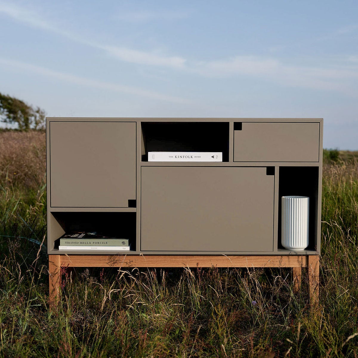 Citti Skåp i färgen Mole Grey. Skåpet står utomhus under blå himmel och i facken står och ligger inredningsdetaljer. 