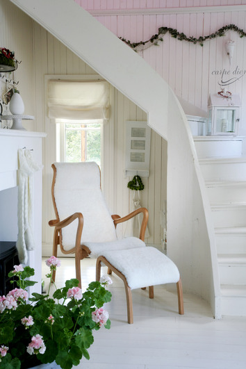 Torparen Fåtölj och Fotpall i fårskinn i ände av vit trappa med en blommande krukväxt i förgrunden