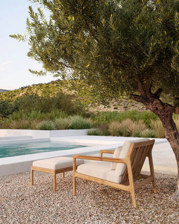 Jack Outdoor Loungefåtölj och fotpall i teak med dynor i färgen Off-White vid poolkant under ett pilträd