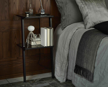 Libri Hylla i svart ask som sängbord bredvid bäddad säng