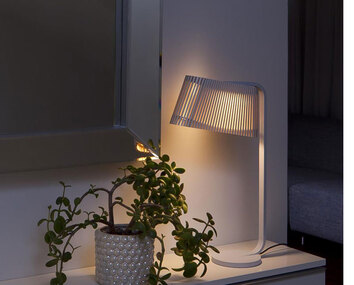 Owalo 7020 Bordslampa tänd i ett mörkt rum bredvid en krukväxt