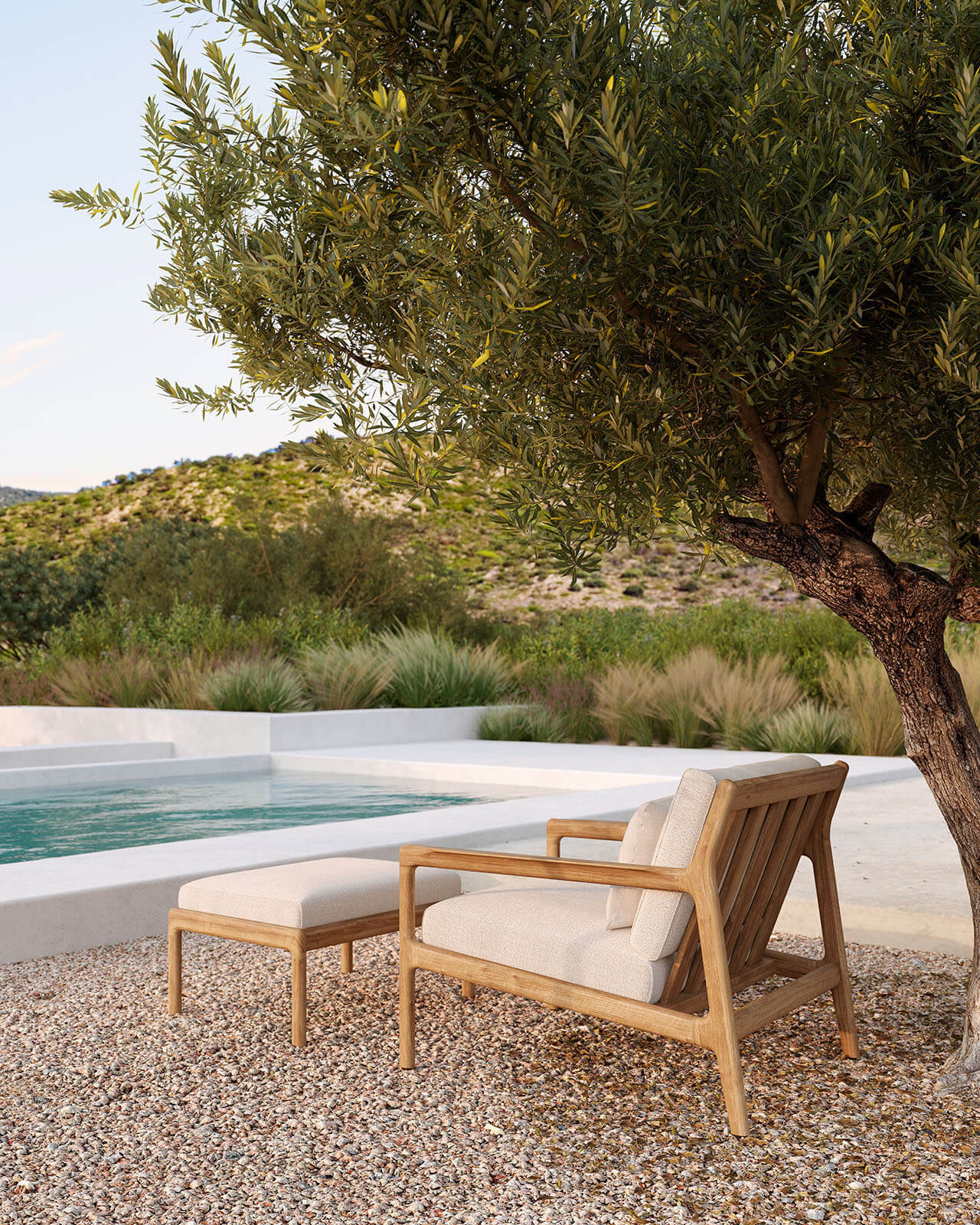 Jack Outdoor Loungefåtölj och fotpall i teak med dynor i färgen Off-White vid poolkant under ett pilträd