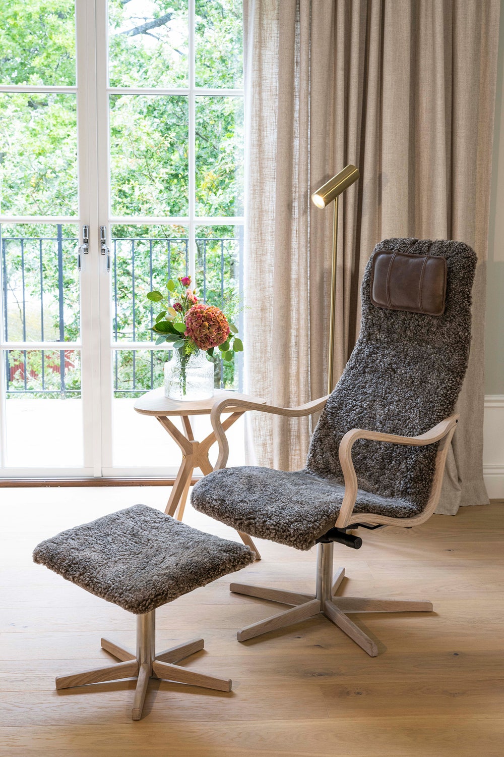 broderna-anderssons-fatolj-chictra-design2.jpg Chic Fåtölj och Fotpall med träfot framför fönster bredvid ett sidobord med blombukett i vas