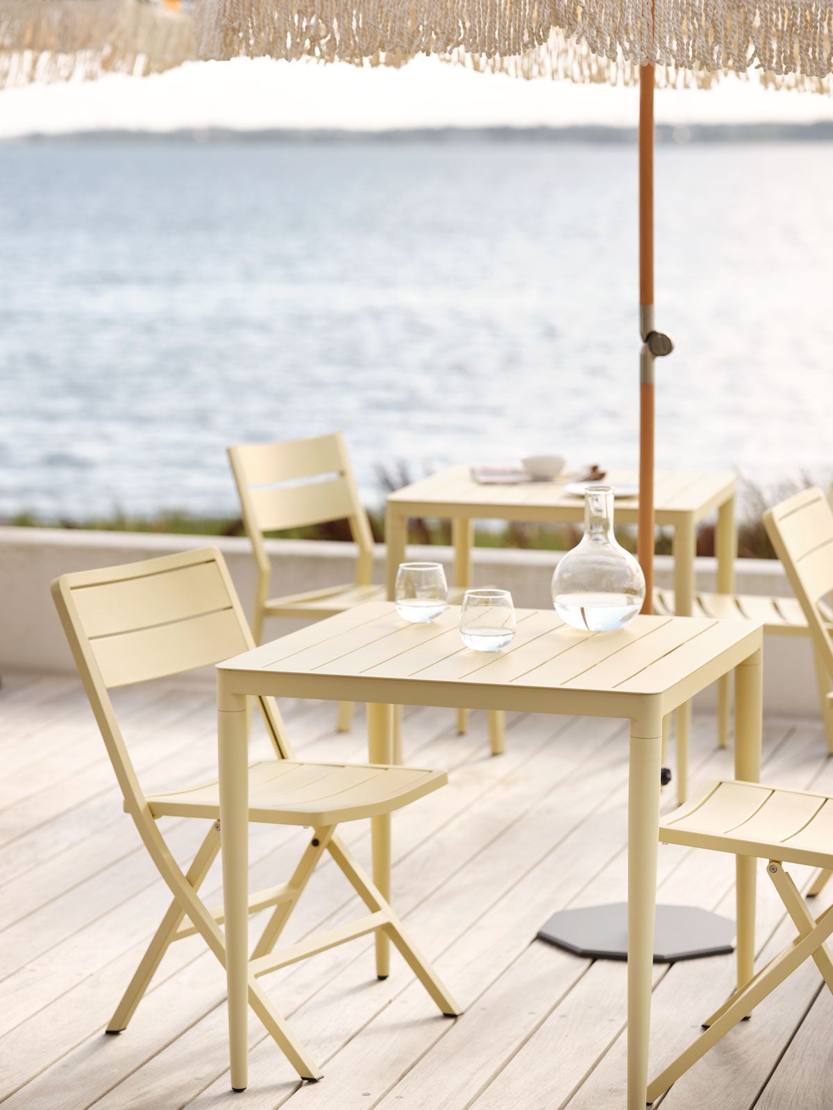 Bigby Matbord 76x76 Gul på trädäck med havsutsikt