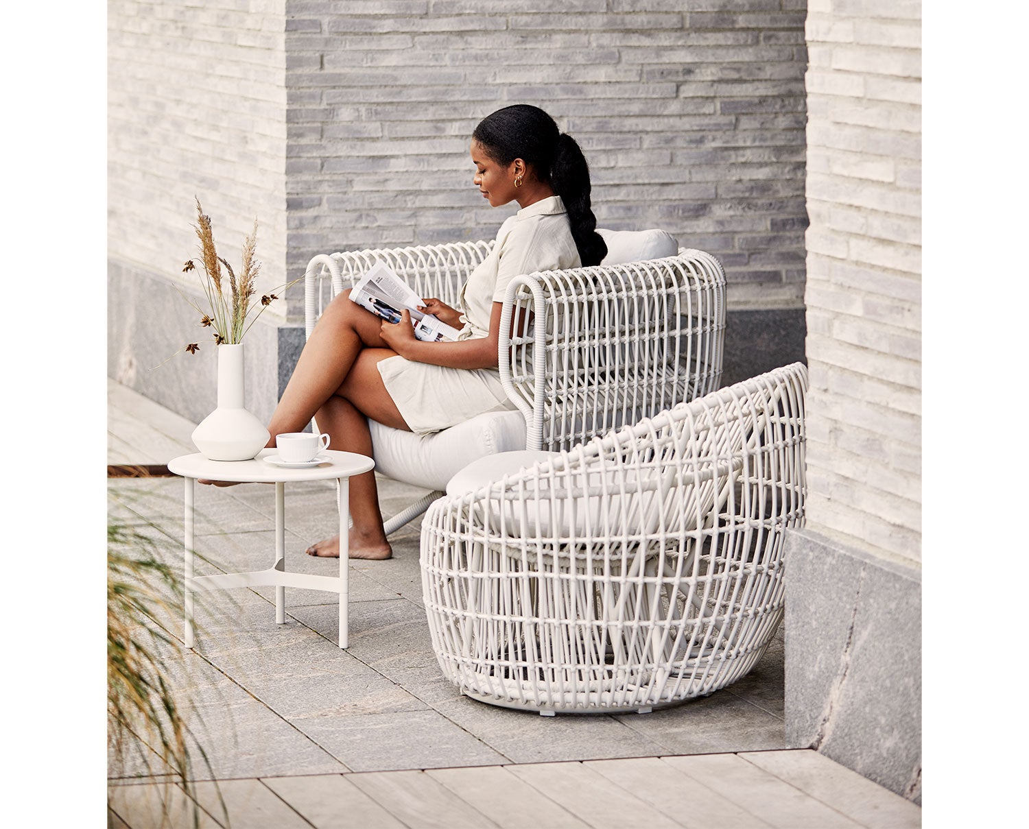 Nest Rund Fåtölj Vit med en kvinna sittande med en öppen tidning
