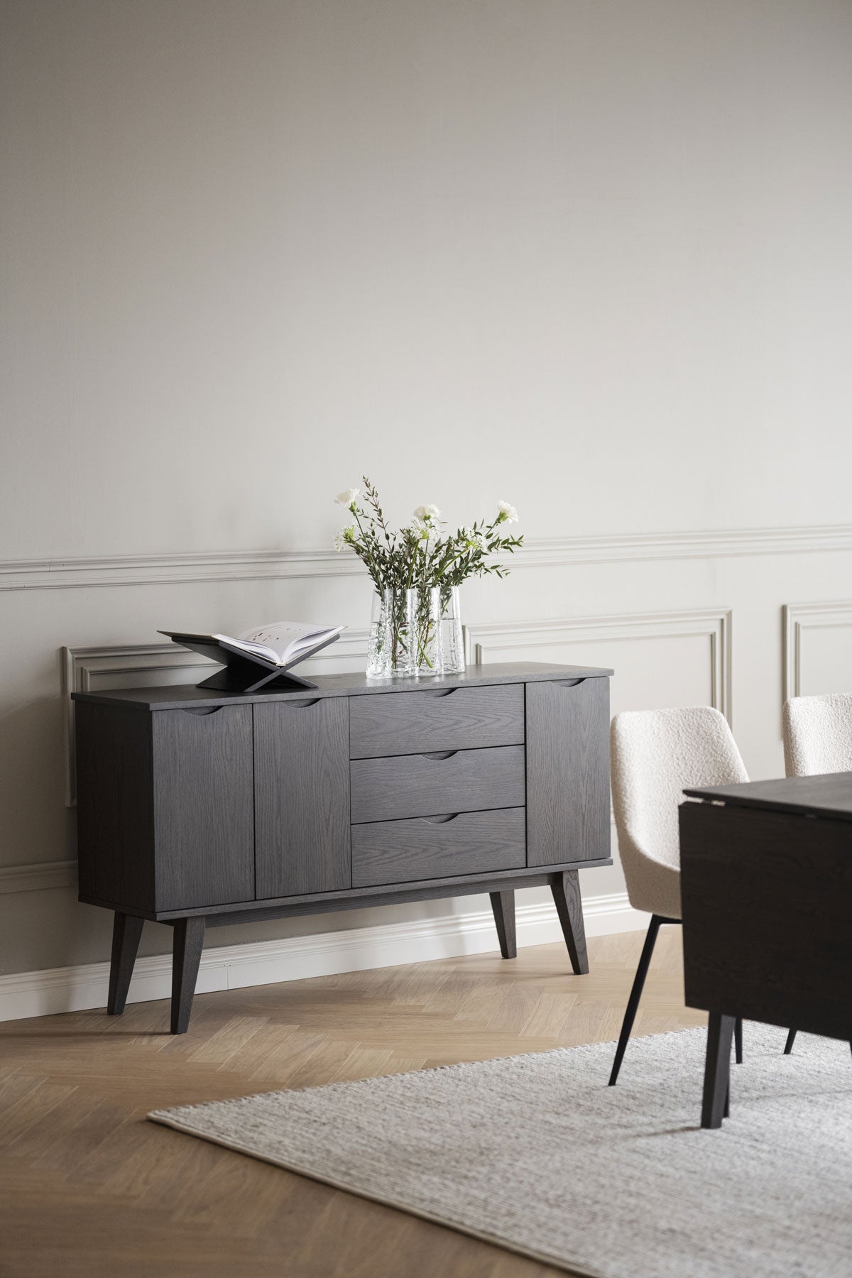 Filippa Sideboard i mörkbrun ek med tidningsställ och en vas med tulpaner