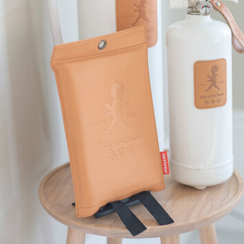 Solstrickans brandfilt i läder ståendes på en pall tillsammans med två vita bradsläckare