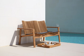 Amaze 2-Sits Soffa intill en pool. Det står en uppdukad bricka framför soffan.