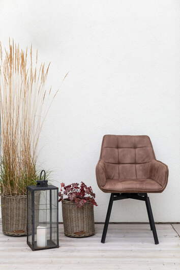 Carro Snurrstol i utomhusmiljö med växter och ljuslykta, klädd i tyget Milla Brun