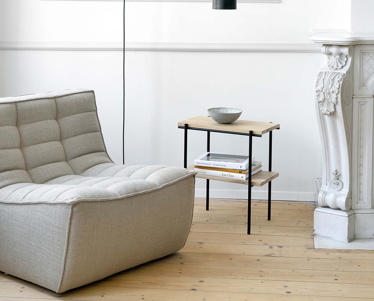 N701 Fåtölj Tyg Beige bredvid ett sidobord med en dekorativ skål och böcker