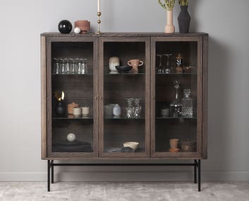 Miljöbild på Velvet vitrinskåp med krukor och vaser bakom de vackra glasdörrarna.