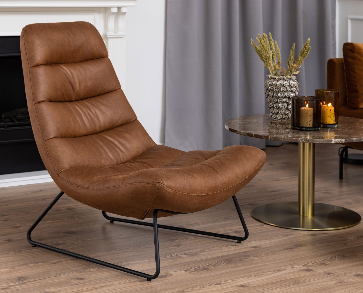 Milford loungefåtölj i Cognac ståendes bredvid sidobord. 