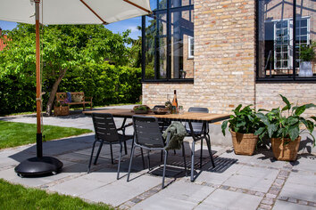 Parc Karmstol runt Parc Trädgårdsbord i solig utomhusmiljö under ett parasoll