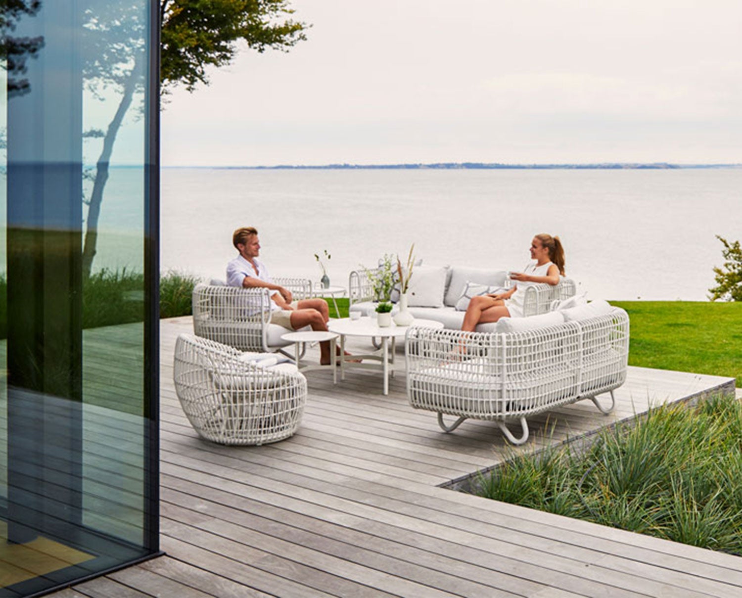 Nest soffgrupp på uteplatsen. Ett par fikar på sin uteplats precis vid havet i Nest soffa och Nest fåtölj i vitt från Cane-line. 