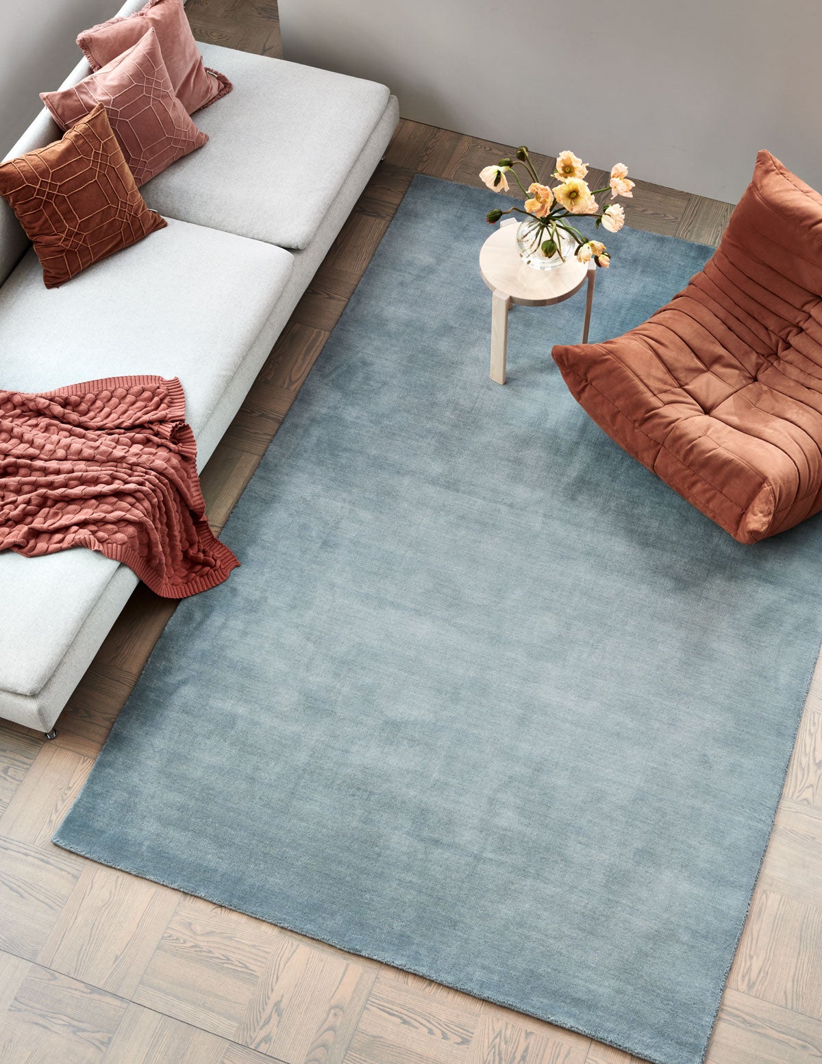 Solid Matta i färgen Blå med orange fåtölj, beige soffa med röda textilier och ett sidobord med en vacker blombukett