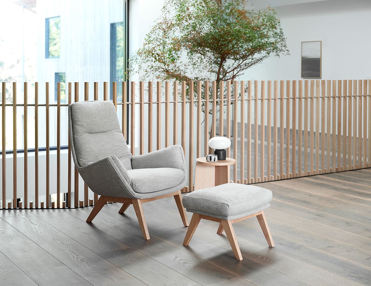 Moro Fåtölj och fotpall i tyget Brescia Calm Grey med ben i ek i ljus kontorsmiljö