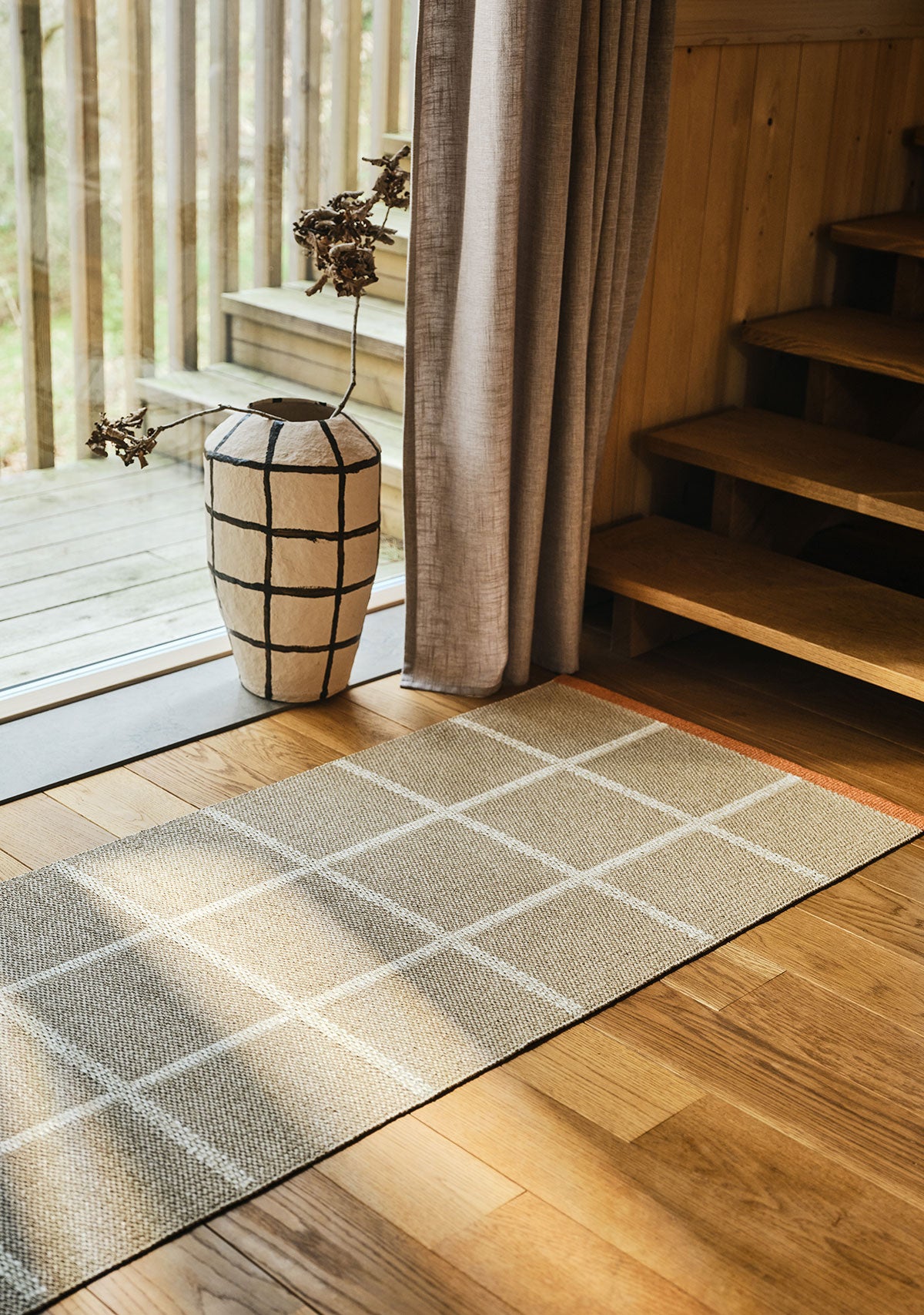 Criss Gångmatta i färgen Beige framför ett fönster med en rutig kruka