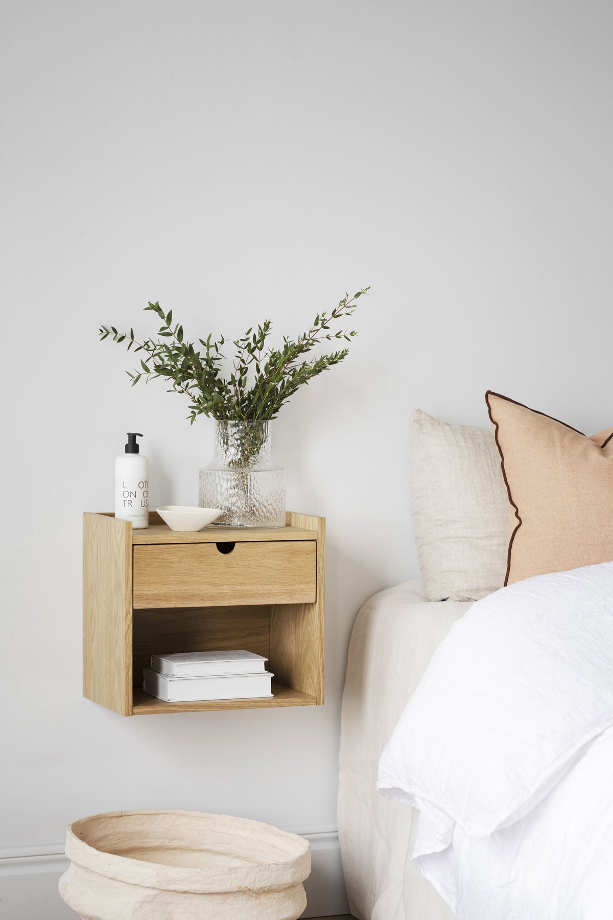 Hillmond Sängbord på vägg bredvid säng med en vas, en skål, en lotion och två böcker