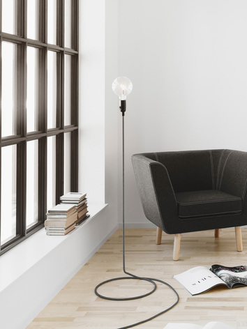 Cord Golvlampa bredvid fåtölj och uppslagen tidning på golvet
