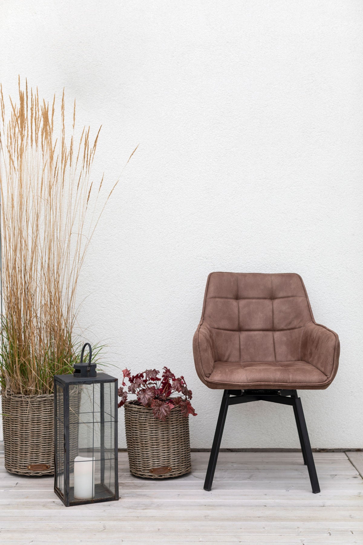 Carro Snurrstol i utomhusmiljö med växter och ljuslykta, klädd i tyget Milla Brun