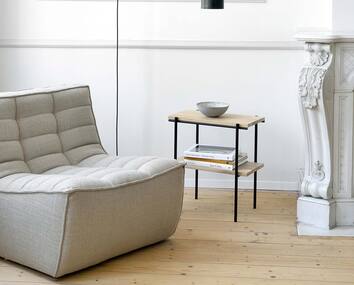 N701 Fåtölj Tyg Beige bredvid ett sidobord med en dekorativ skål och böcker