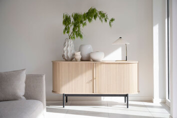 Ljuset strilar in på Haddington Sideboard i ljus ek i ett ljust vardagsrum med vita väggar och beige soffa.