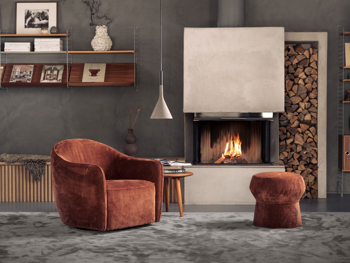 Fåtöljen Beetle i vardagsrumsmiljö, tillsammans med en tänd eldstad.