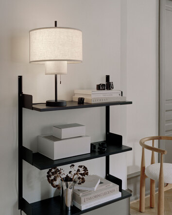 New Works Vägghylla 900 Svart med bordslampa, böcker, boxar och vas med blommor