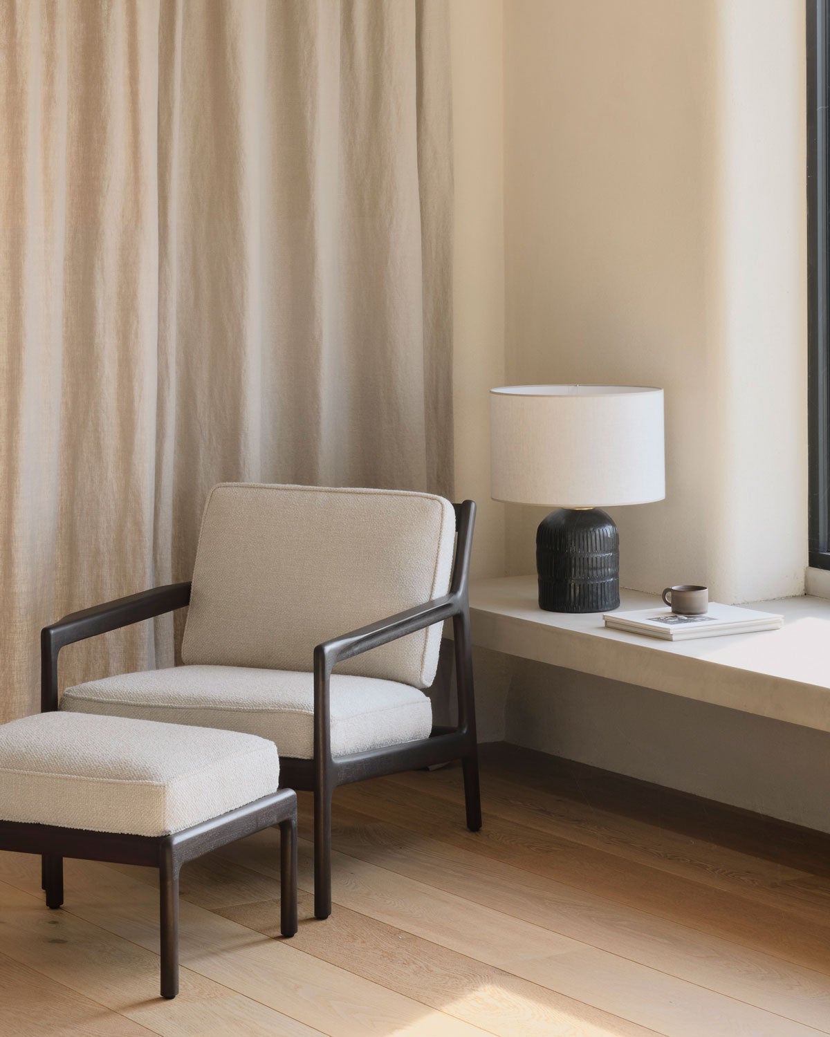 Jack Loungestol och Fotpall klädda i tyget Ivory, bredvid en fönsterkarm dekorerad med en bordslampa och en tidning