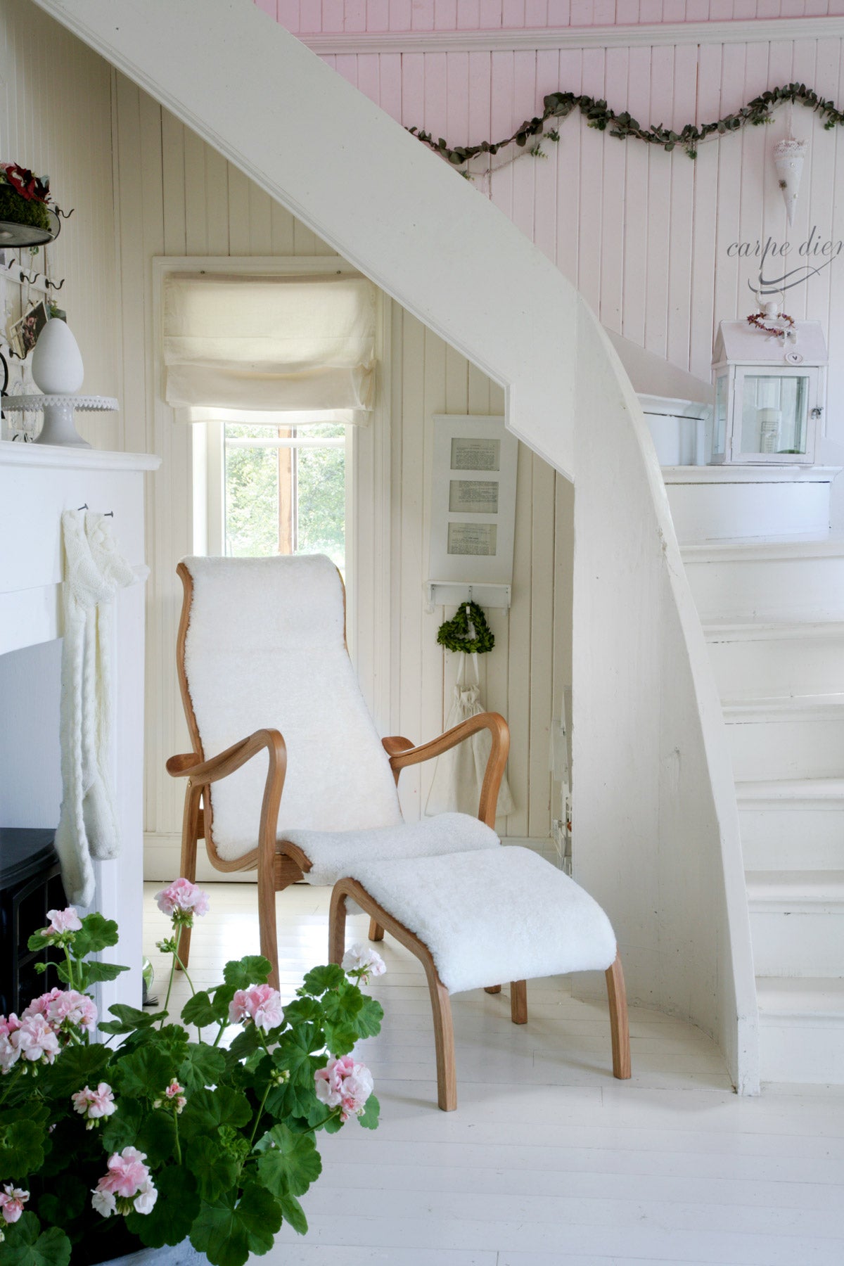 Torparen Fåtölj och Fotpall i fårskinn i ände av vit trappa med en blommande krukväxt i förgrunden