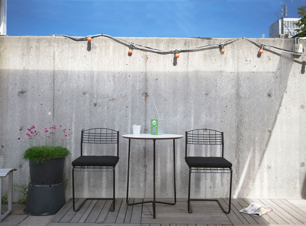 High Tech Stol Svart runt High Tech Bord 60 mot betongvägg på soligt trädäck