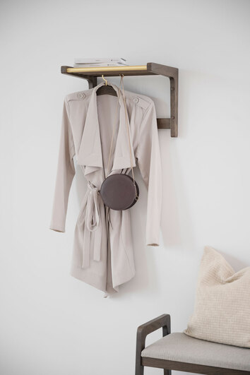 Miljöbild på Inverness Hatthylla 45 cm i rökt ek och  mässing upphängd i en liten hall med en ljus kappa med och en brun handväska hängandes på en galge. 