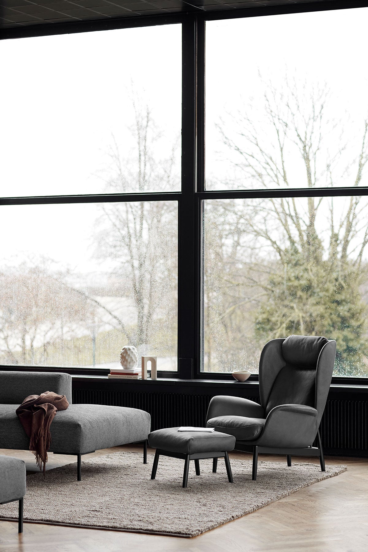 Padova Fåtölj och fotpall i lädret Nature Warm Stone Grey med svarta ben i modernt vardagsrum