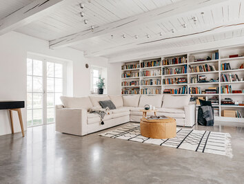 Kibo Hörnsoffa i beige tyg framför inbyggda bokhyllor fulla med böcker