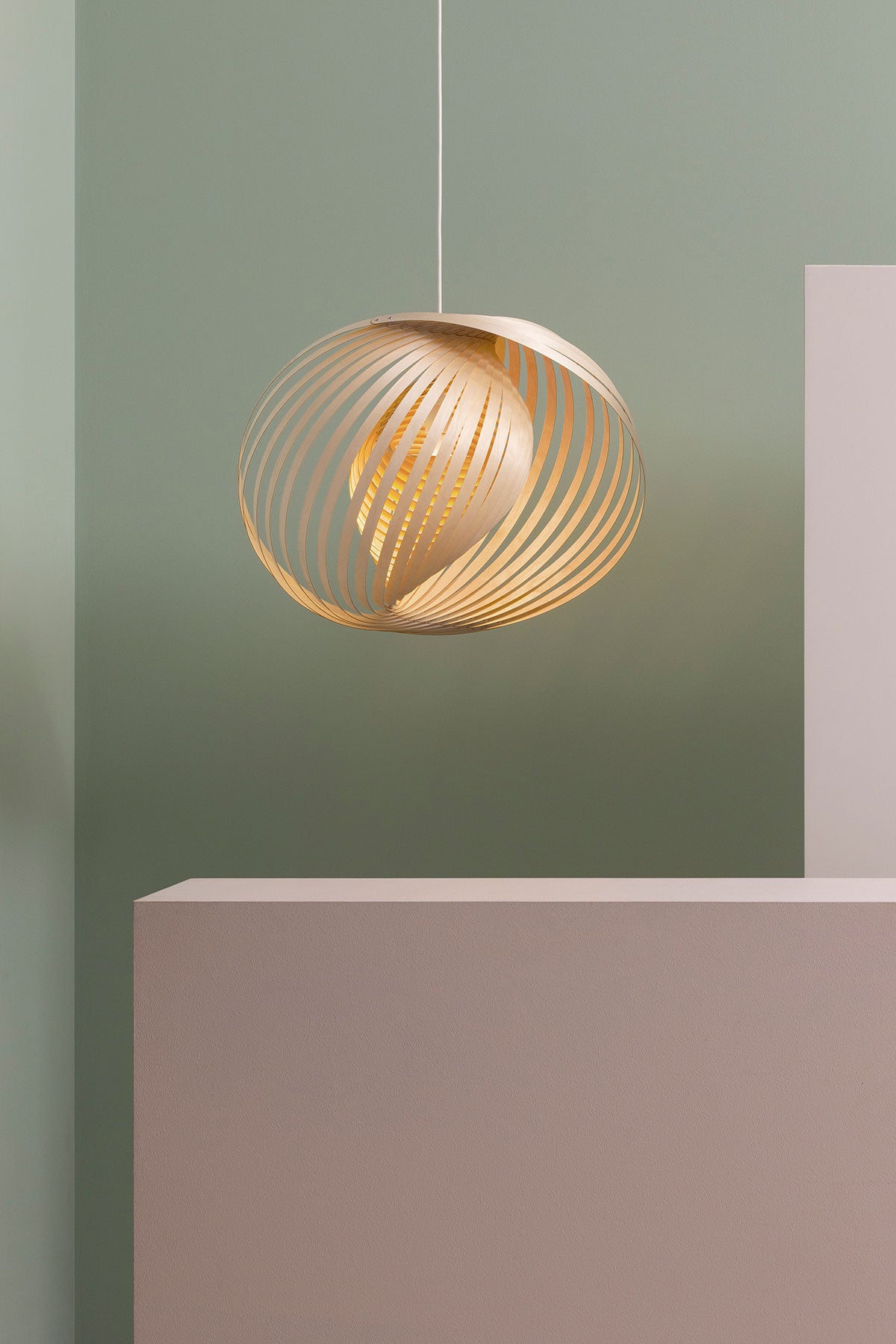 Adilo 8200 Taklampa i björk som hänger mot en ljusgrön vägg