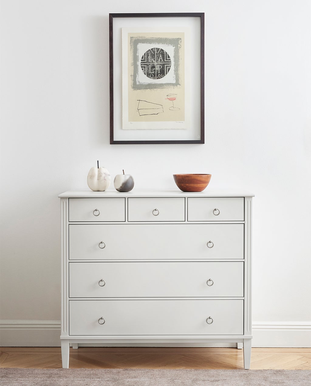 Stockholm 2.0 Byrå Whitewash med dekorativa detaljer nedanför en vägghängd tavla