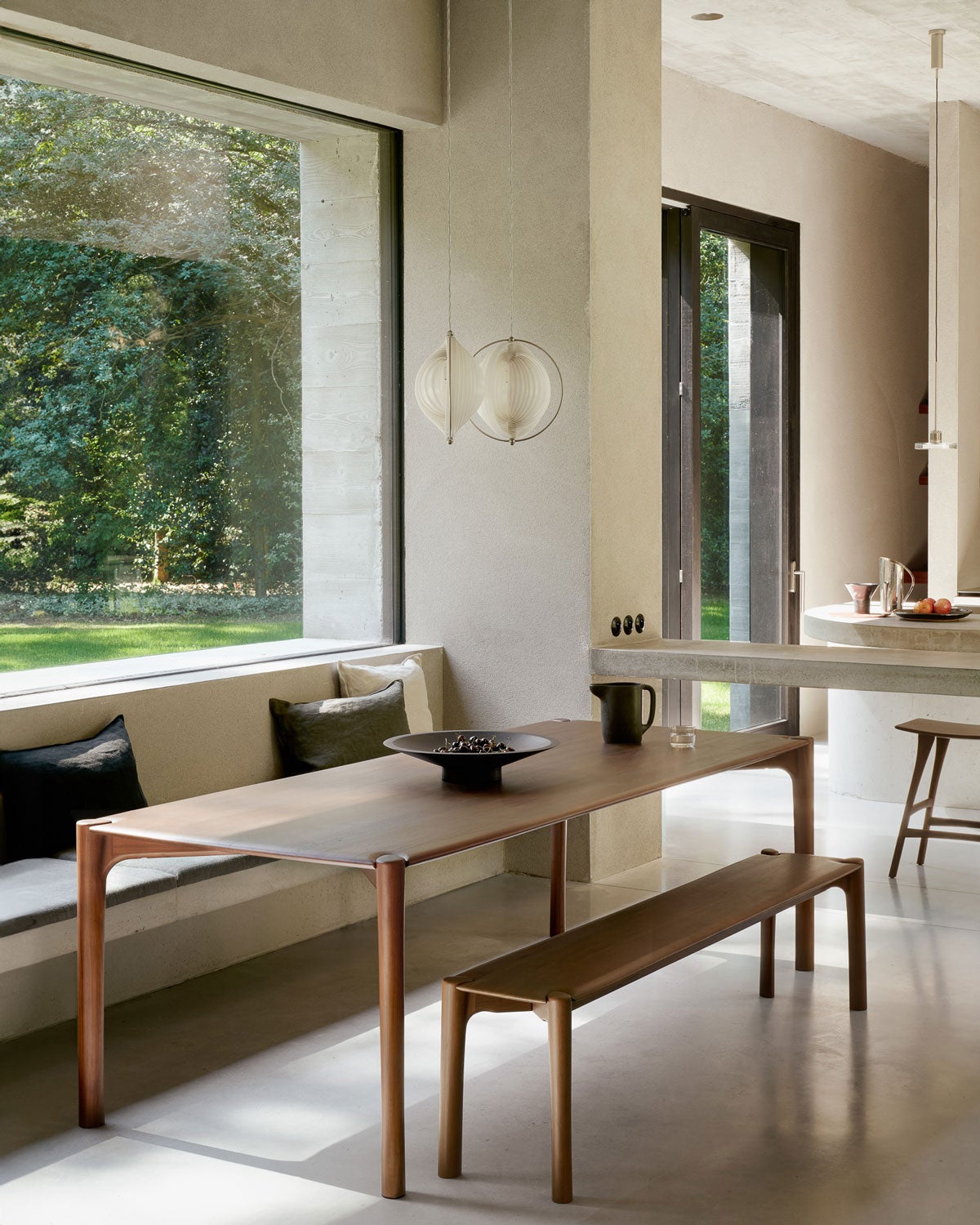 PI Bänk och Matbord i brunlackad teak vid fönster som vetter ut mot grönskande miljö