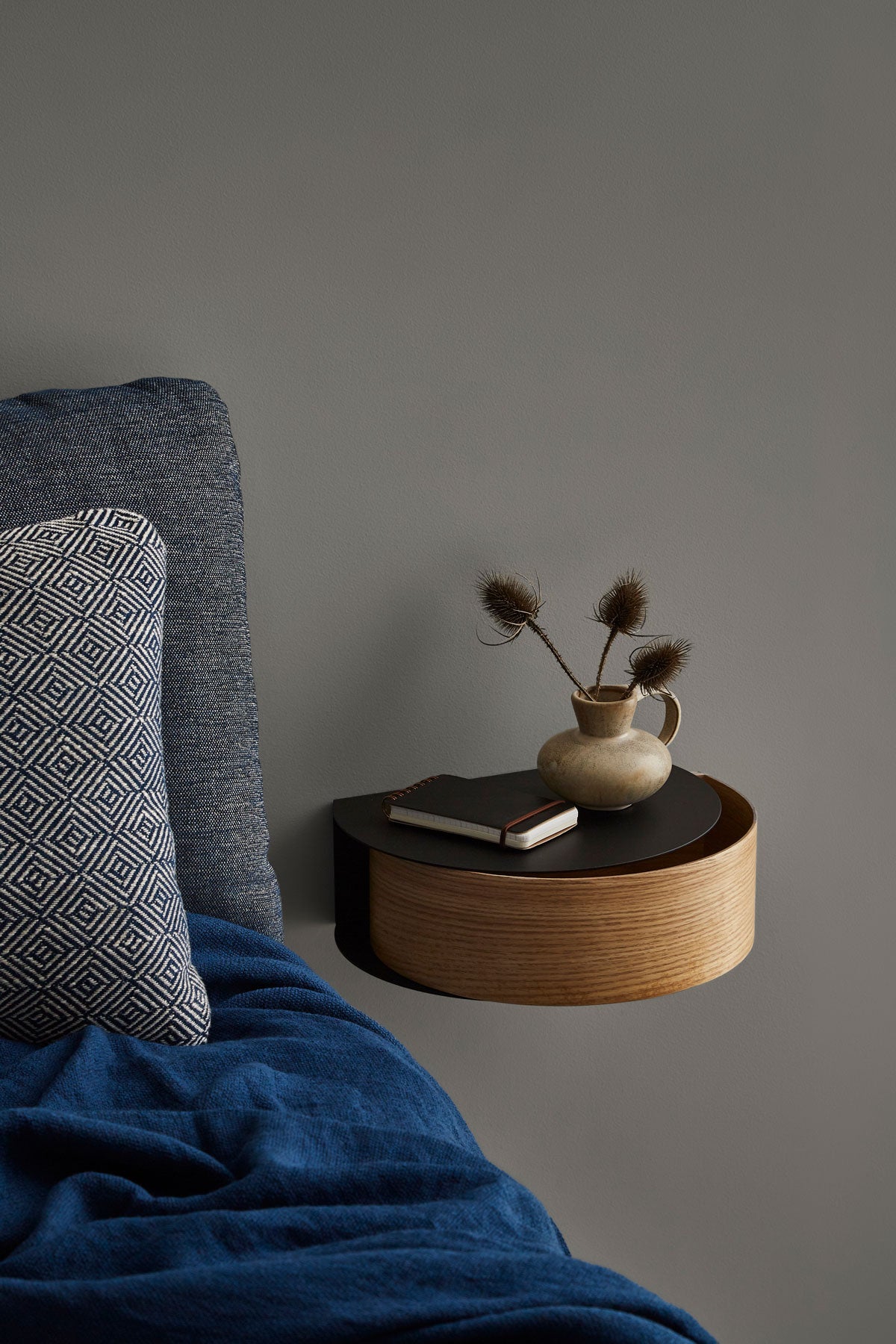 Wallie Vägghylla Vitpigmenterad Ek / Svart som sängbord bredvid bäddad säng