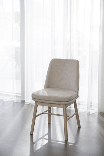 Amesbury Stol Vitpigmenterad Ek i ljusbeige tyg framför skira gardiner