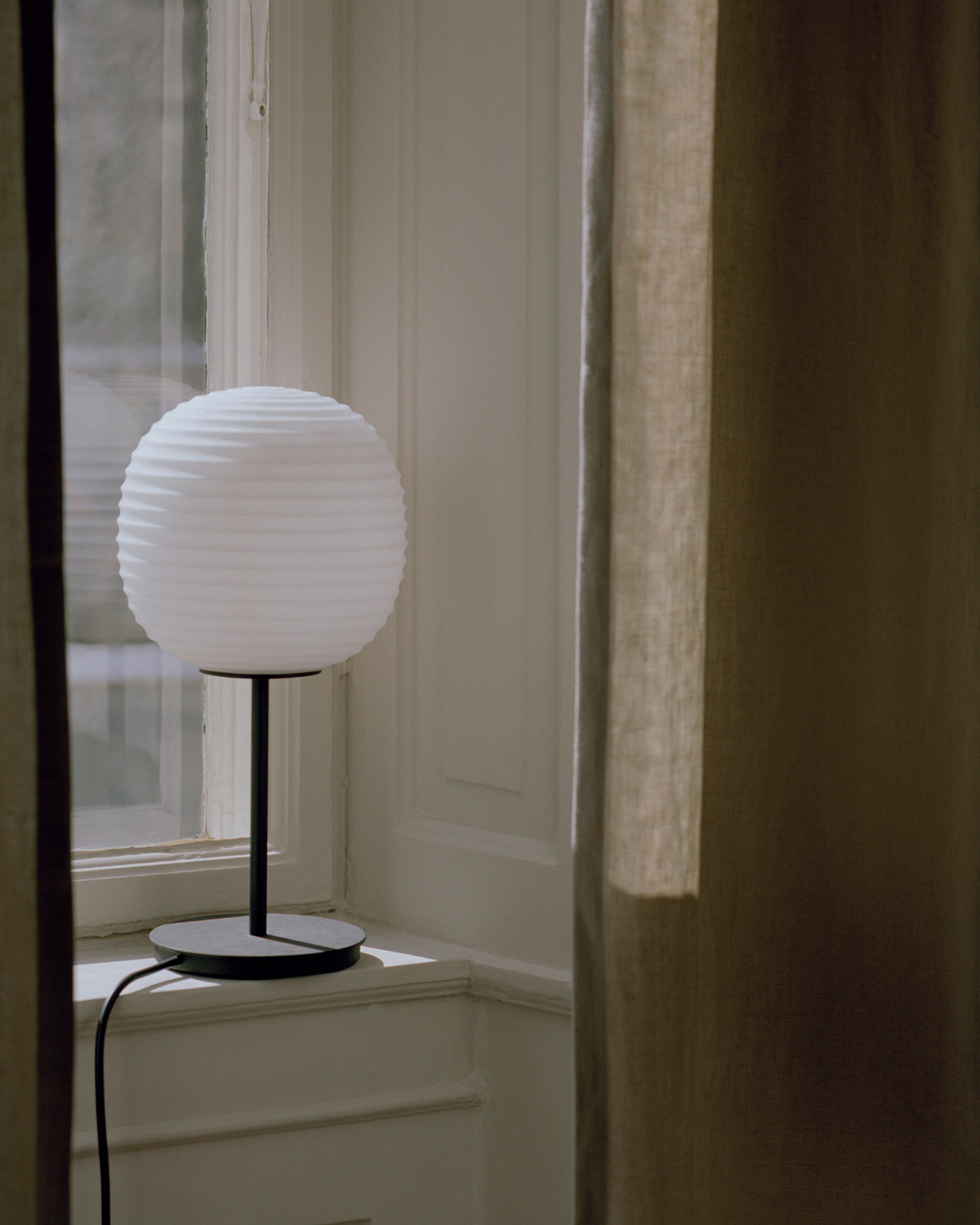 Terra Bordslampa från New Works i fönster med bruna gardiner