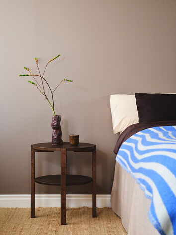 Solo Fåtöljbord i rökt ek, bredvid en bäddad säng